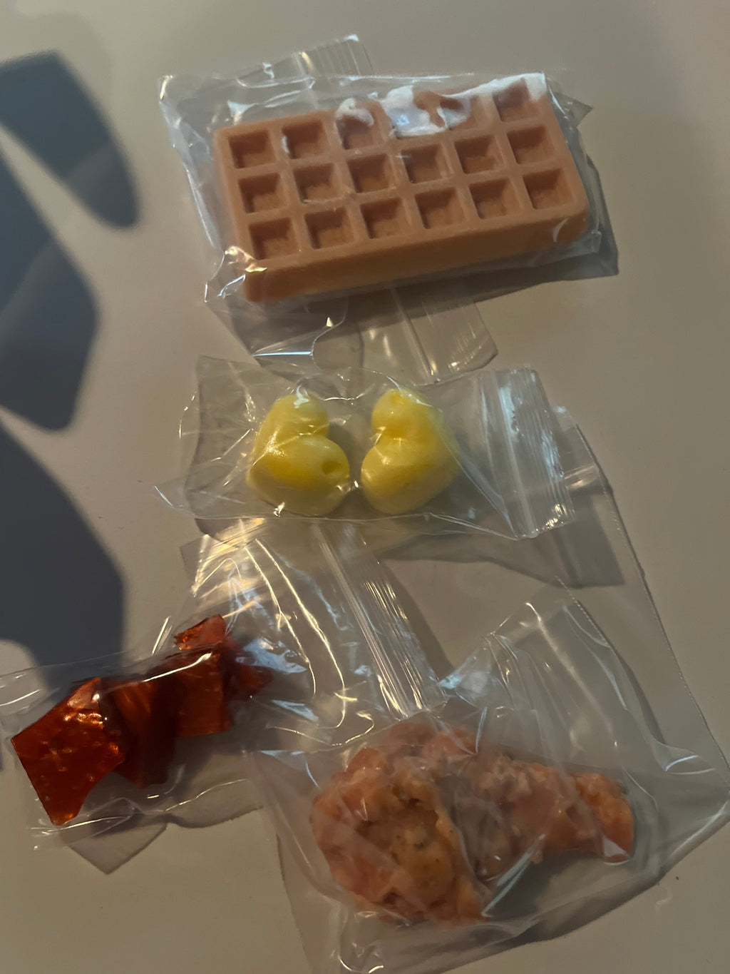 Small wax melt food items in clear plastic packages on a white surface