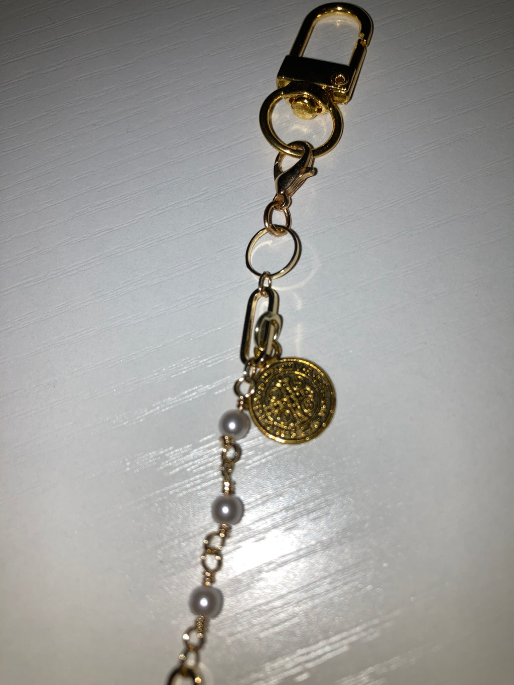 A close-up of a gold-tone chain bracelet featuring a small gold flower charm and a pink enamel lip charm, resting on a white surface.
