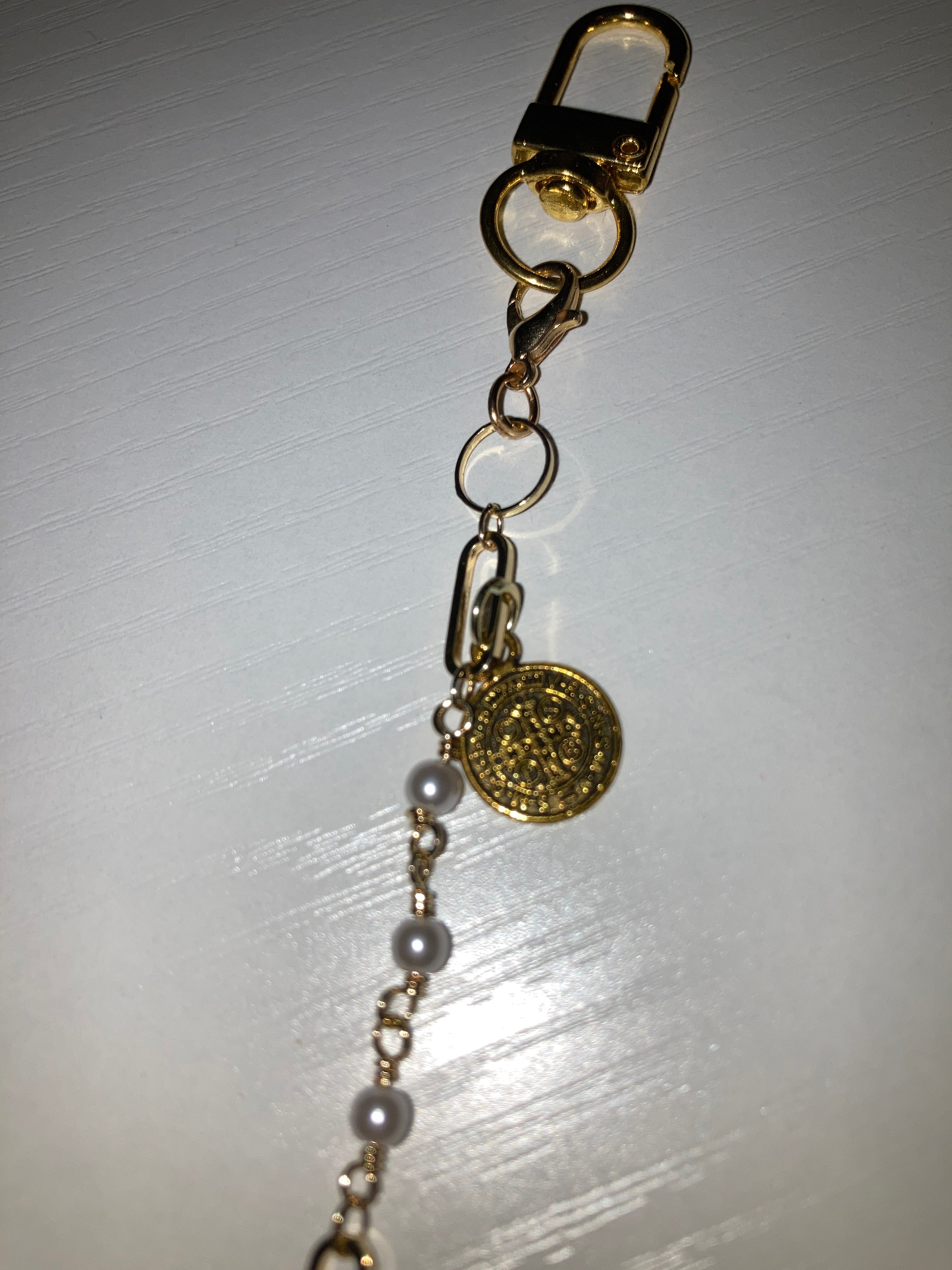 A close-up of a gold-tone chain bracelet featuring a small gold flower charm and a pink enamel lip charm, resting on a white surface.