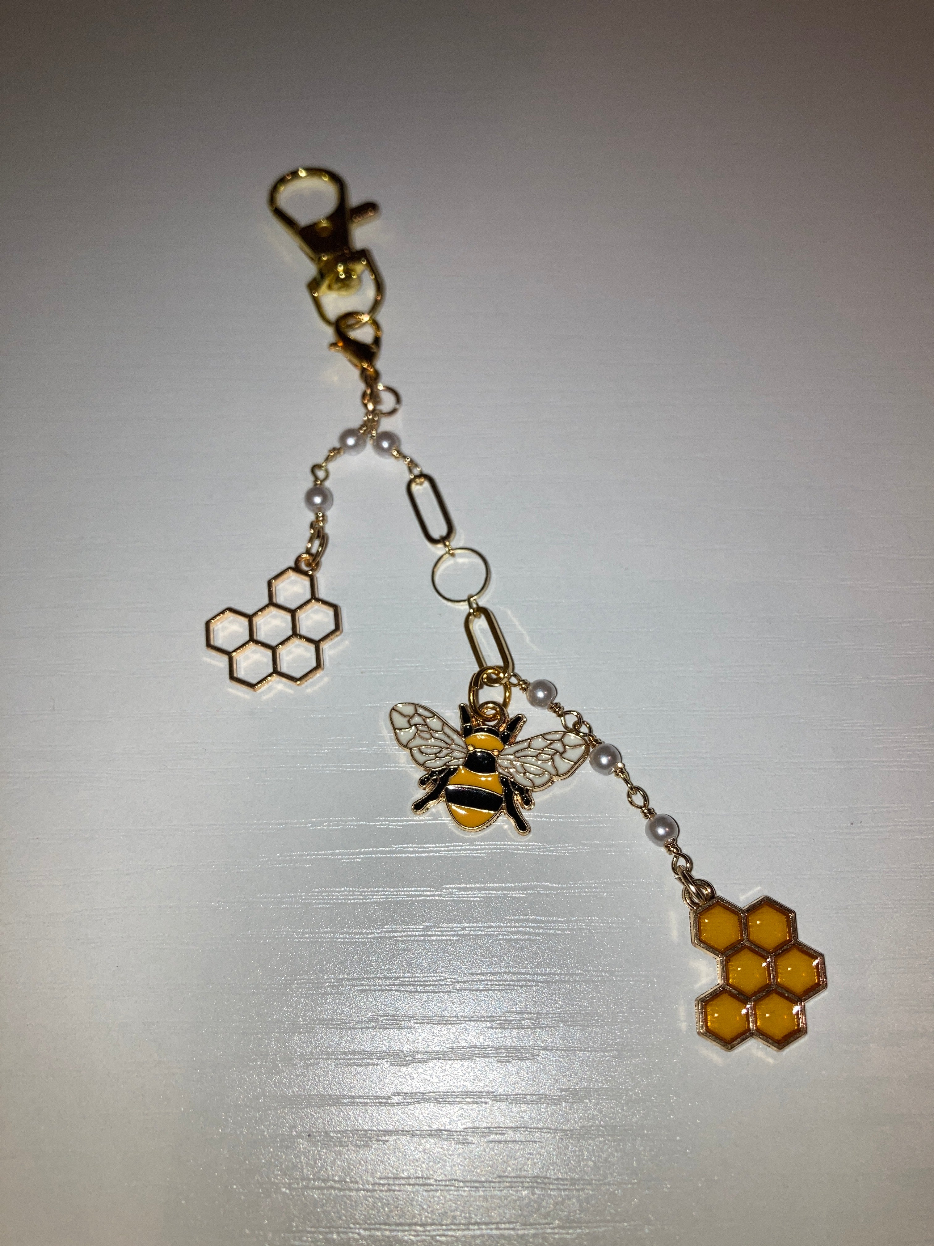 A gold-tone beehive charm with a lobster clasp, featuring a bee charm, honeycomb details, and small clear beads on a light gray background.